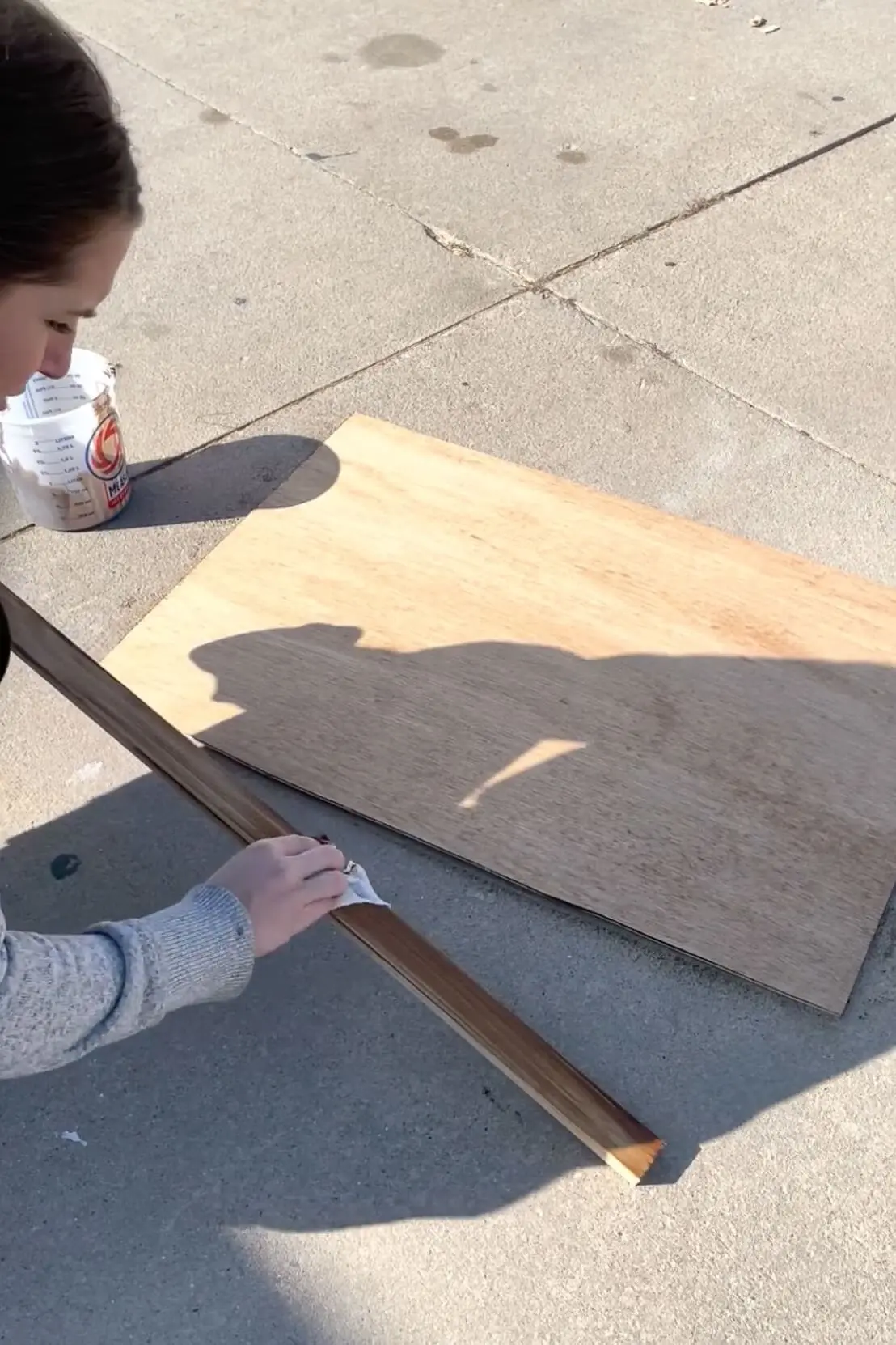 A DIYer applies wood stain to a trim piece and to plywood.